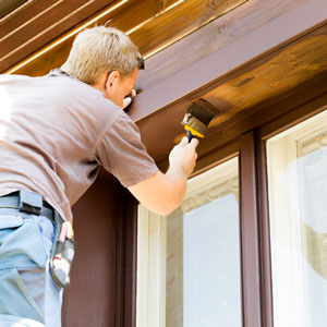 Mann streicht Fensterrahmen aus Holz mit Pinsel und Lasur ohne zu tropfen